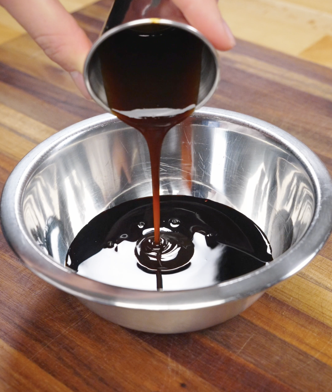 Dark soy-based sauce being poured into a metal mixing bowl, combining ingredients for Thai basil ground beef sauce.