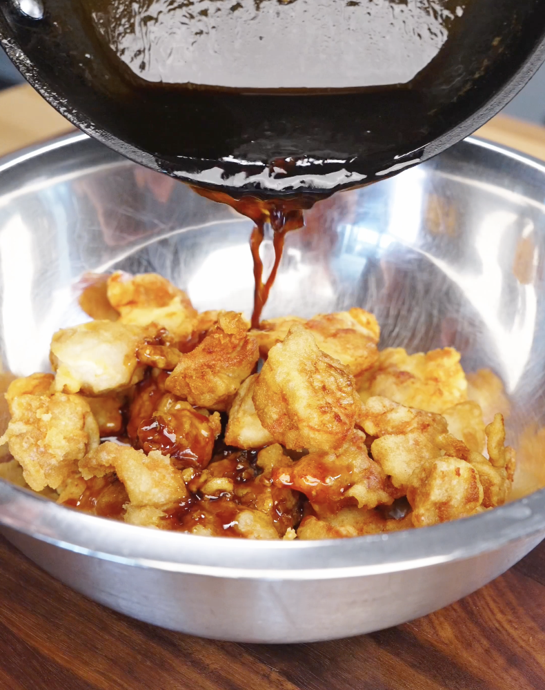 Thick honey butter sauce being poured over crispy fried chicken in a bowl, coating each piece evenly.
