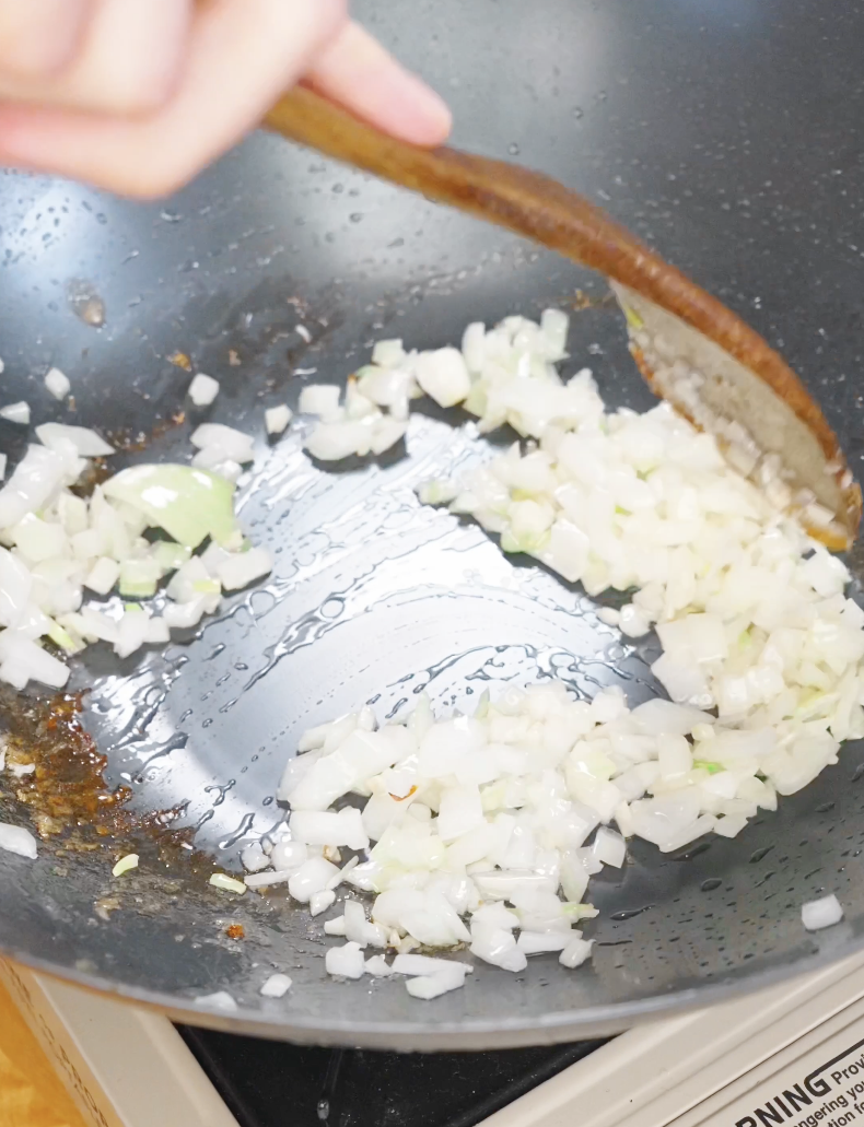 Finely diced onions being saut&eacute;ed in a pan with oil, building the aromatic base for chicken fried rice.