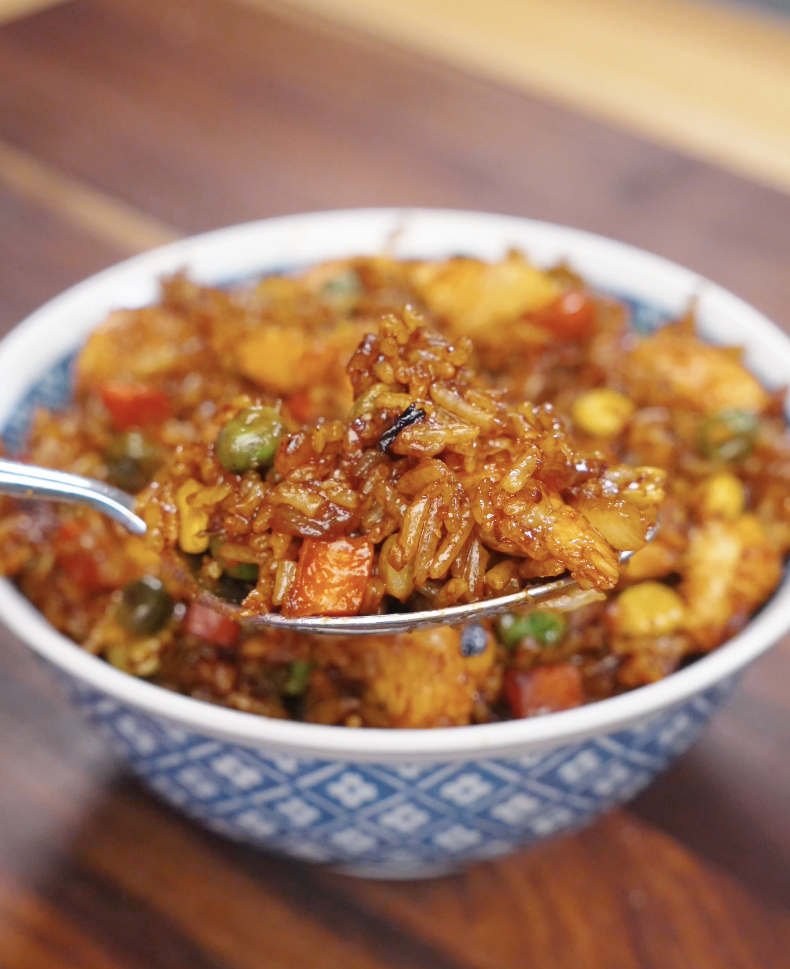 Spoon lifting chicken fried rice from a bowl, showing fluffy grains of rice mixed with chicken and vegetables.