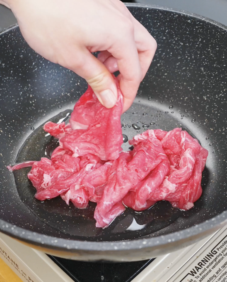 Thinly sliced raw beef being placed into a hot pan with oil to sear for the Beef Chow Mein Recipe.