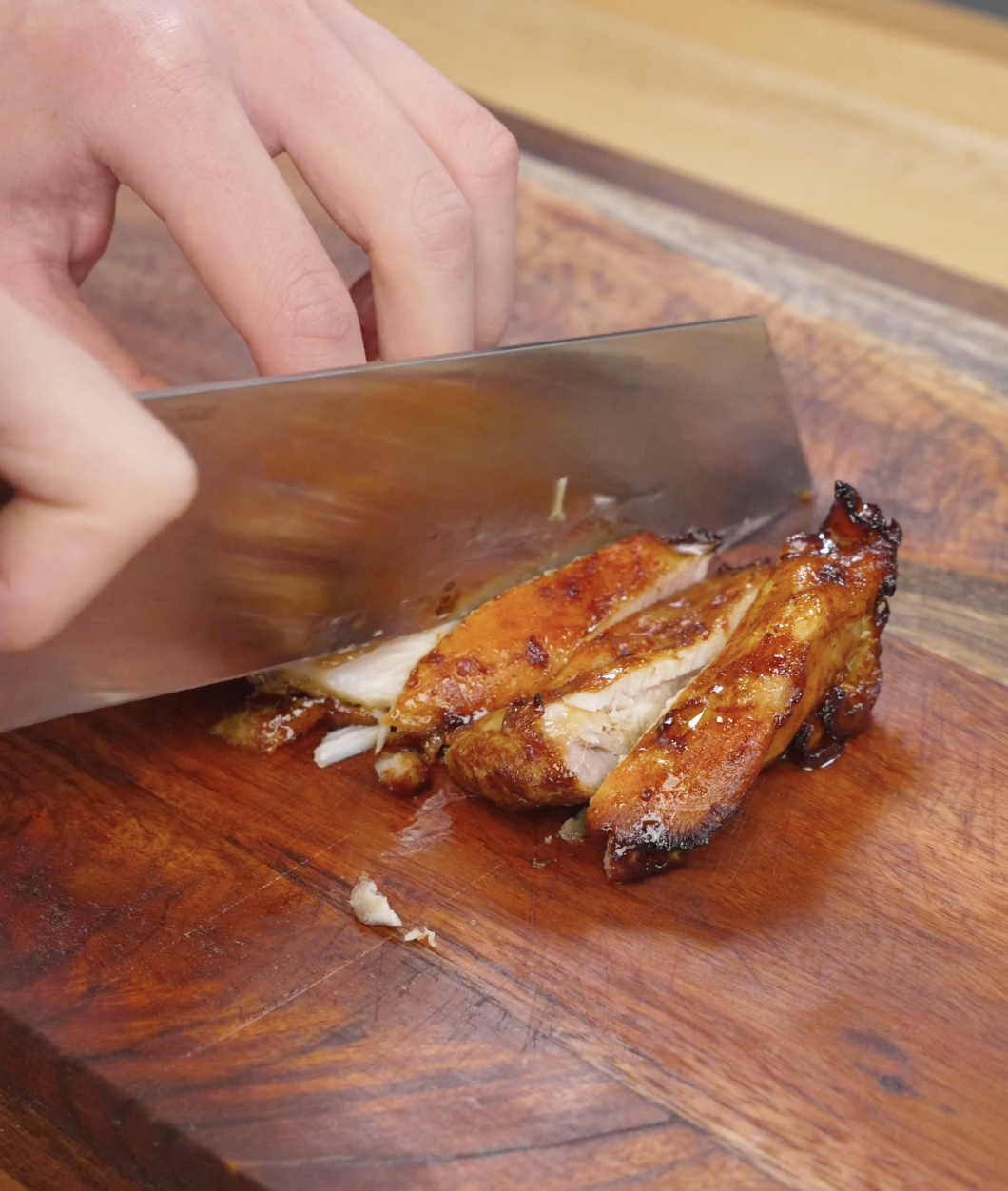 Cooked chicken bulgogi being sliced into thin strips on a wooden cutting board, revealing juicy interior and caramelized exterior from the marinade.