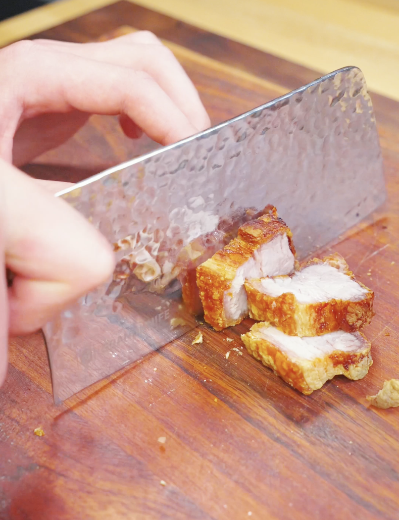Crispy pork belly being sliced into bite-sized pieces on a cutting board, showing crunchy skin and tender layers in the Vietnamese Crispy Pork Belly Recipe.