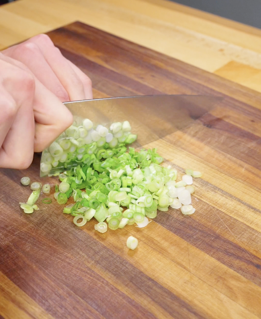 Knife slicing fresh scallions on a cutting board for garlic bacon fried rice preparation.