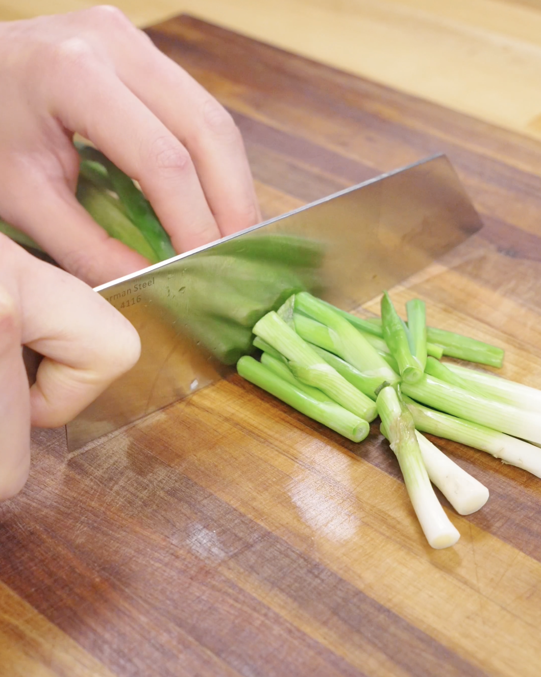 Fresh scallions being cut into segments on a wooden cutting board, prepping aromatics for chicken chow mein.