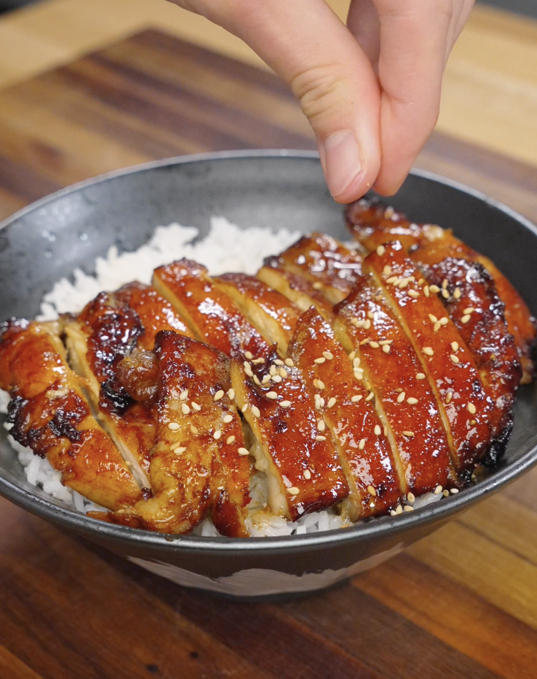 Sesame seeds being sprinkled over sliced chicken bulgogi on top of rice, adding texture and nutty flavor to the finished dish.