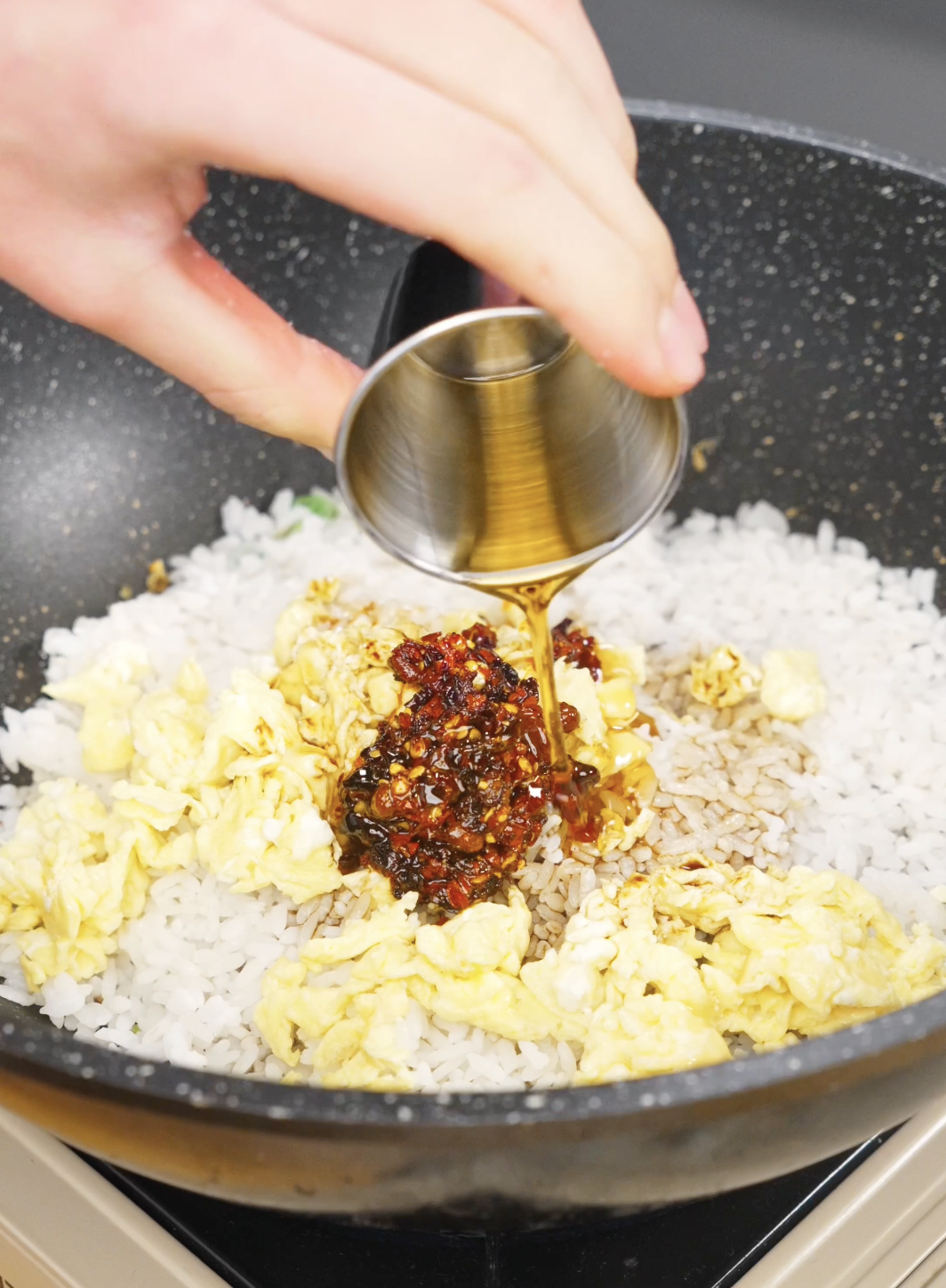 Chili oil and soy sauce mixture being poured over rice and scrambled eggs in a skillet to season this spicy Chili Oil Butter Fried Rice Recipe.