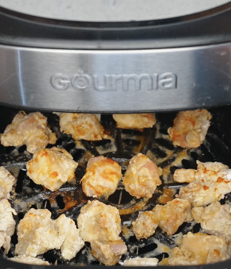 Chicken thigh pieces cooking inside an air fryer until golden brown and crispy. Air frying creates crunchy chicken bites with less oil while keeping the inside tender and juicy.