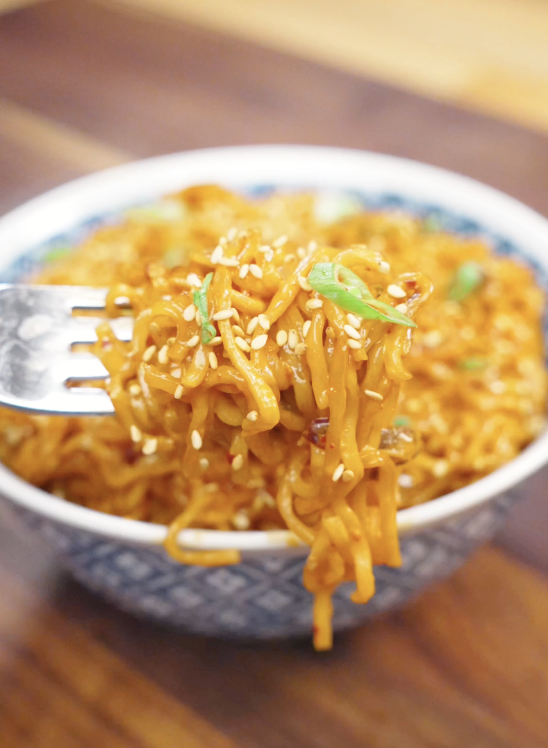Fork lifting creamy chili oil noodles coated in a glossy spicy cream sauce with sesame seeds and scallions for the perfect comforting noodle bite.
