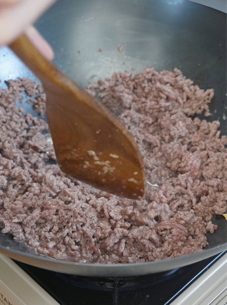 Ground beef being broken apart and cooked in a wok for the Japanese Ground Beef Egg Bowl Recipe.