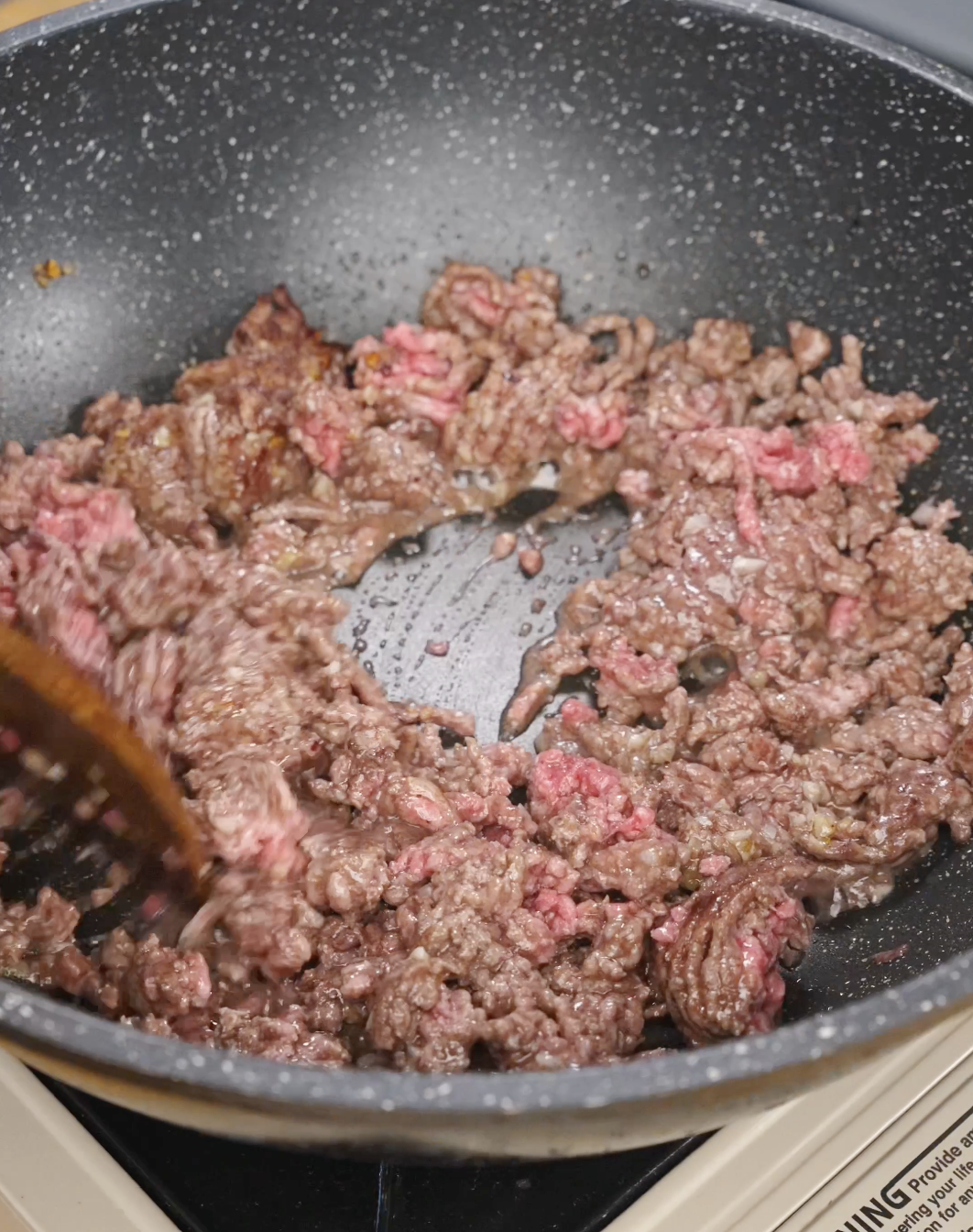 Ground beef cooking in a skillet while being broken apart with a wooden spoon for this quick and flavorful Sticky Ground Beef Recipe.