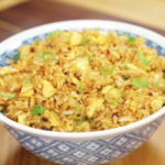 Bowl of Chili Oil Butter Fried Rice topped with scallions featuring fluffy eggs, glossy rice grains, garlic, and spicy chili oil for an easy comfort food dinner recipe.