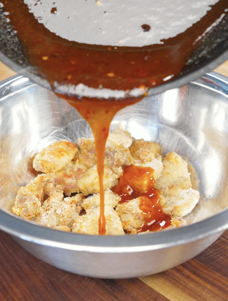 Freshly cooked hot honey sauce being poured over crispy air-fried chicken pieces in a mixing bowl. Tossing the chicken in the glaze evenly coats every piece with sweet, spicy, and savory flavor.