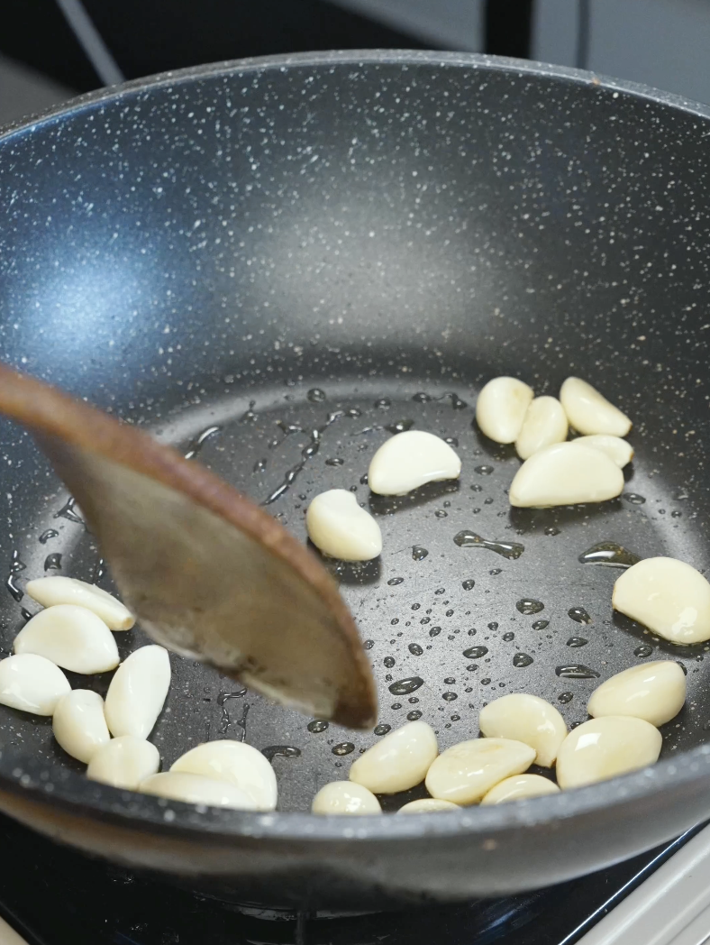 Whole peeled garlic cloves saut&eacute;ing in oil inside a pan until lightly golden for the Whole Garlic Chicken Stir Fry Recipe.
