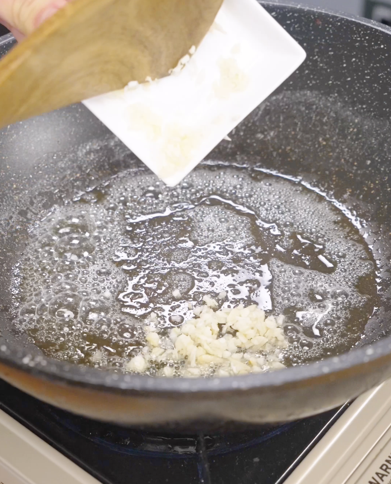 Minced garlic being added to melted butter in a skillet while making Gochujang Butter Noodles. Cooking the garlic in butter creates a rich aromatic base that builds flavor throughout the dish.