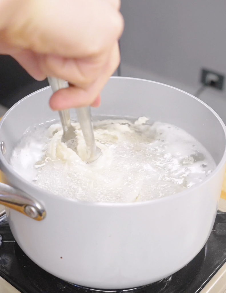Wide noodles being stirred in a pot of boiling water while cooking for Gochujang Butter Noodles. Cooking the noodles just before al dente helps them finish perfectly in the spicy butter sauce.
