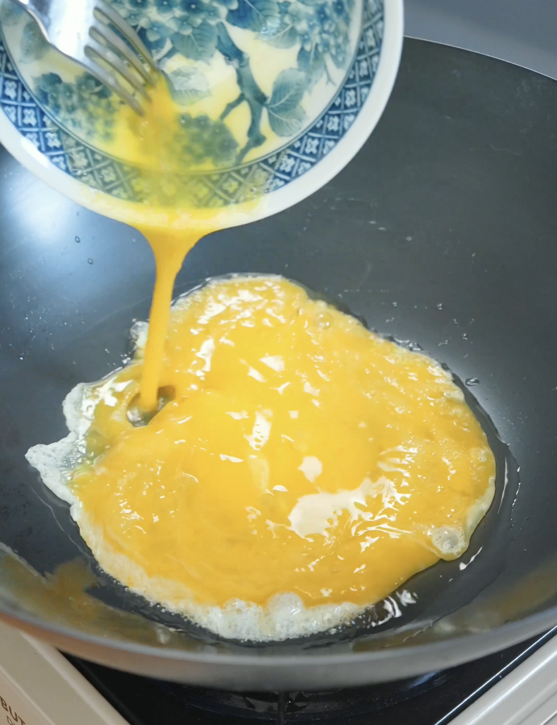 Whisked eggs being poured into a hot wok to make soft scrambled eggs for the Japanese Ground Beef Egg Bowl Recipe.