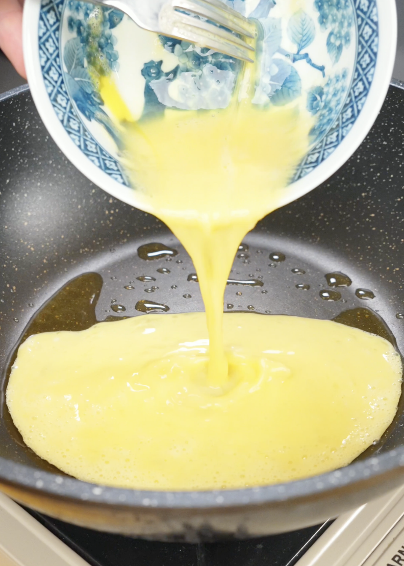 Whisked eggs being poured into a lightly oiled skillet to make fluffy scrambled eggs for Egg Fried Rice. Cooking the eggs separately helps maintain their texture and prevents them from overcooking.