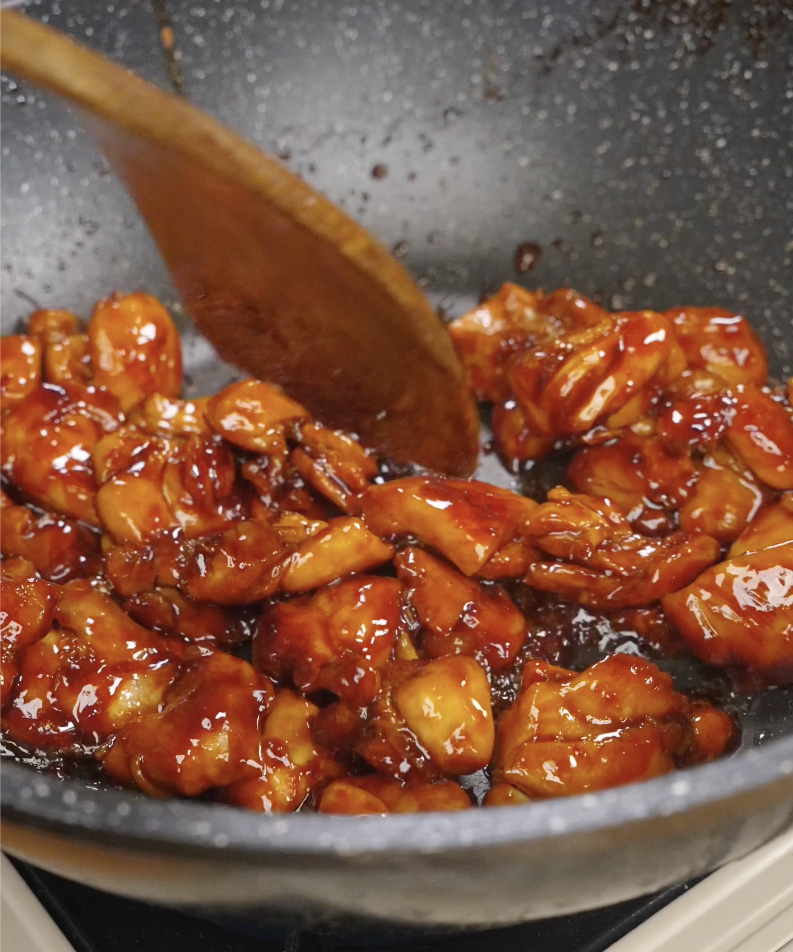 Chicken thigh pieces cooking in a skillet as the marinade reduces into a thick sticky sauce. Simmering the chicken directly in the marinade allows the glaze to caramelize and cling to every piece.