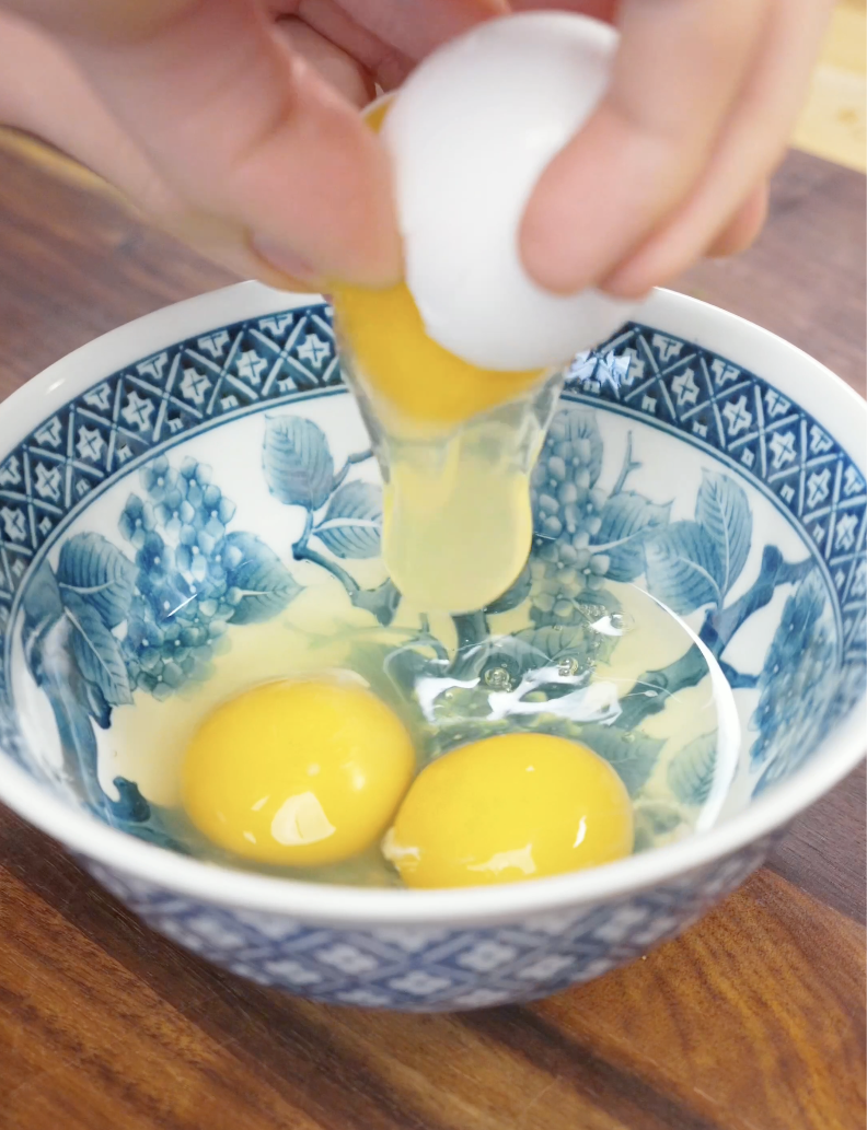 Eggs being cracked into a bowl before whisking for Egg Fried Rice. Using beaten eggs creates soft, fluffy egg pieces that mix evenly throughout the fried rice.