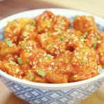 Finished bowl of Crispy Gochujang Chicken coated in a glossy sweet and spicy gochujang glaze and garnished with sesame seeds and scallions. This easy air fryer chicken recipe delivers restaurant-quality flavor with a crispy exterior and tender juicy chicken.