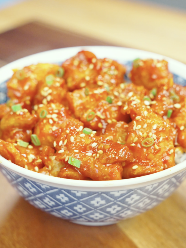 Finished bowl of Crispy Gochujang Chicken coated in a glossy sweet and spicy gochujang glaze and garnished with sesame seeds and scallions. This easy air fryer chicken recipe delivers restaurant-quality flavor with a crispy exterior and tender juicy chicken.