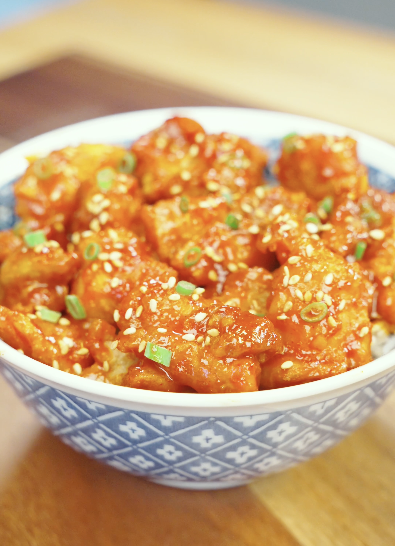 Finished bowl of Crispy Gochujang Chicken coated in a glossy sweet and spicy gochujang glaze and garnished with sesame seeds and scallions. This easy air fryer chicken recipe delivers restaurant-quality flavor with a crispy exterior and tender juicy chicken.