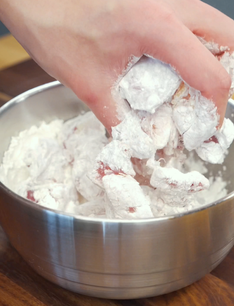 Chicken thigh pieces being coated in a mixture of cornstarch, flour, and salt before air frying. This light dredge helps create the crispy texture that makes this Crispy Gochujang Chicken Recipe so satisfying.