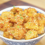 Bowl of Crispy Hot Honey Chicken served over steamed rice and topped with sesame seeds and sliced scallions. The sticky hot honey sauce creates the perfect balance of sweetness, spice, and crunch in this easy weeknight dinner.