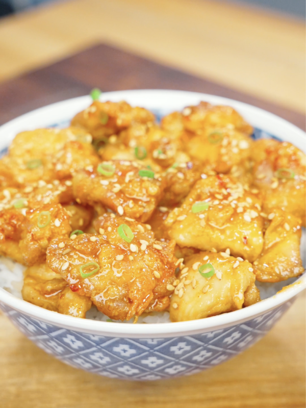 Bowl of Crispy Hot Honey Chicken served over steamed rice and topped with sesame seeds and sliced scallions. The sticky hot honey sauce creates the perfect balance of sweetness, spice, and crunch in this easy weeknight dinner.