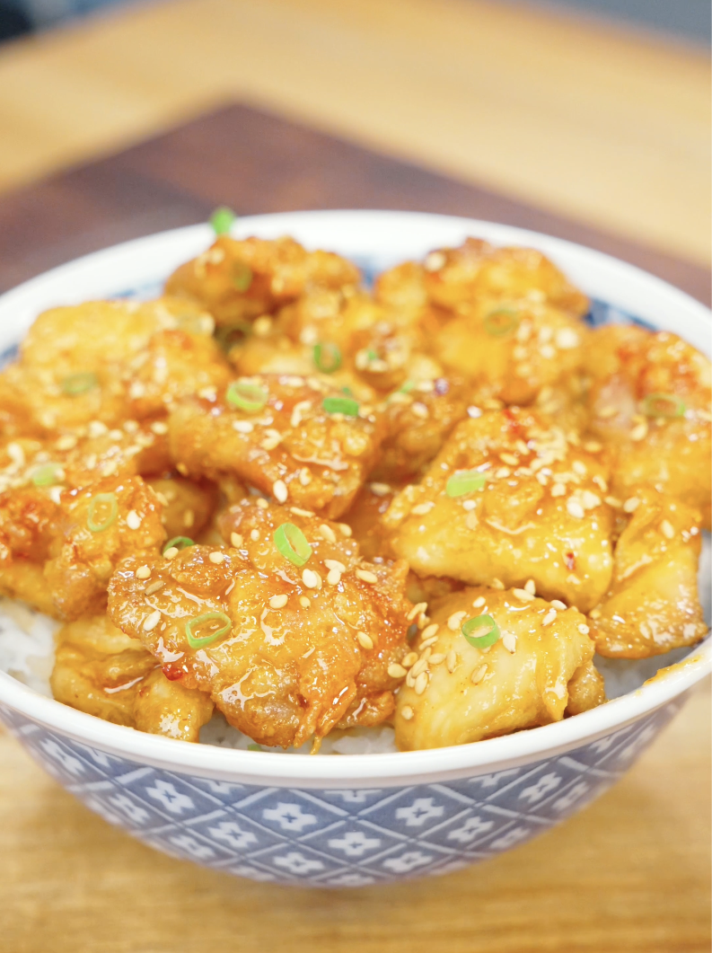 Bowl of Crispy Hot Honey Chicken served over steamed rice and topped with sesame seeds and sliced scallions. The sticky hot honey sauce creates the perfect balance of sweetness, spice, and crunch in this easy weeknight dinner.