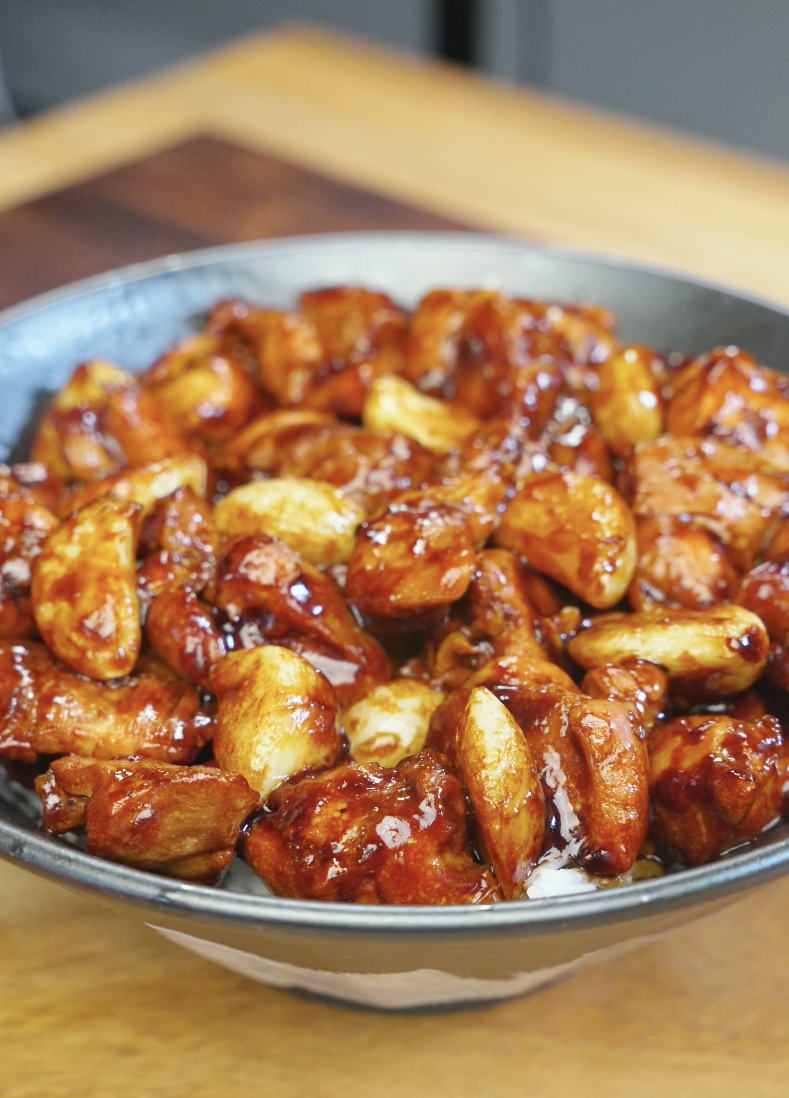 Bowl of glossy chicken thighs and softened whole garlic cloves coated in a thick savory sauce in the Whole Garlic Chicken Stir Fry Recipe.