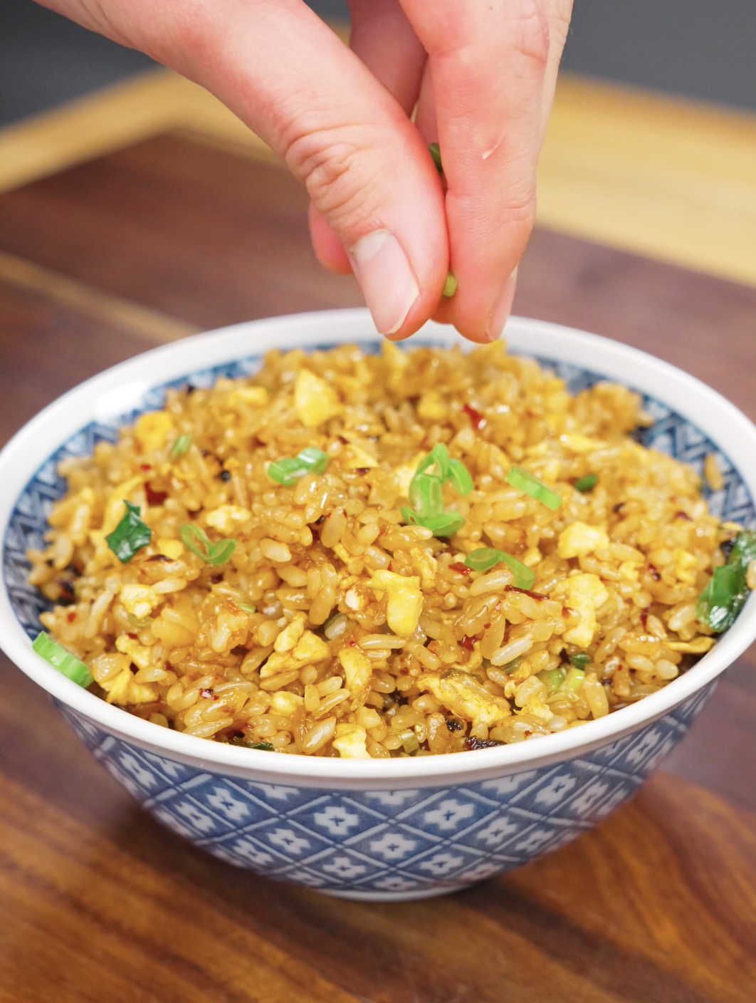 Fresh scallions being sprinkled over a bowl of Chili Oil Butter Fried Rice Recipe as a final garnish for this savory and spicy weeknight rice dish.
