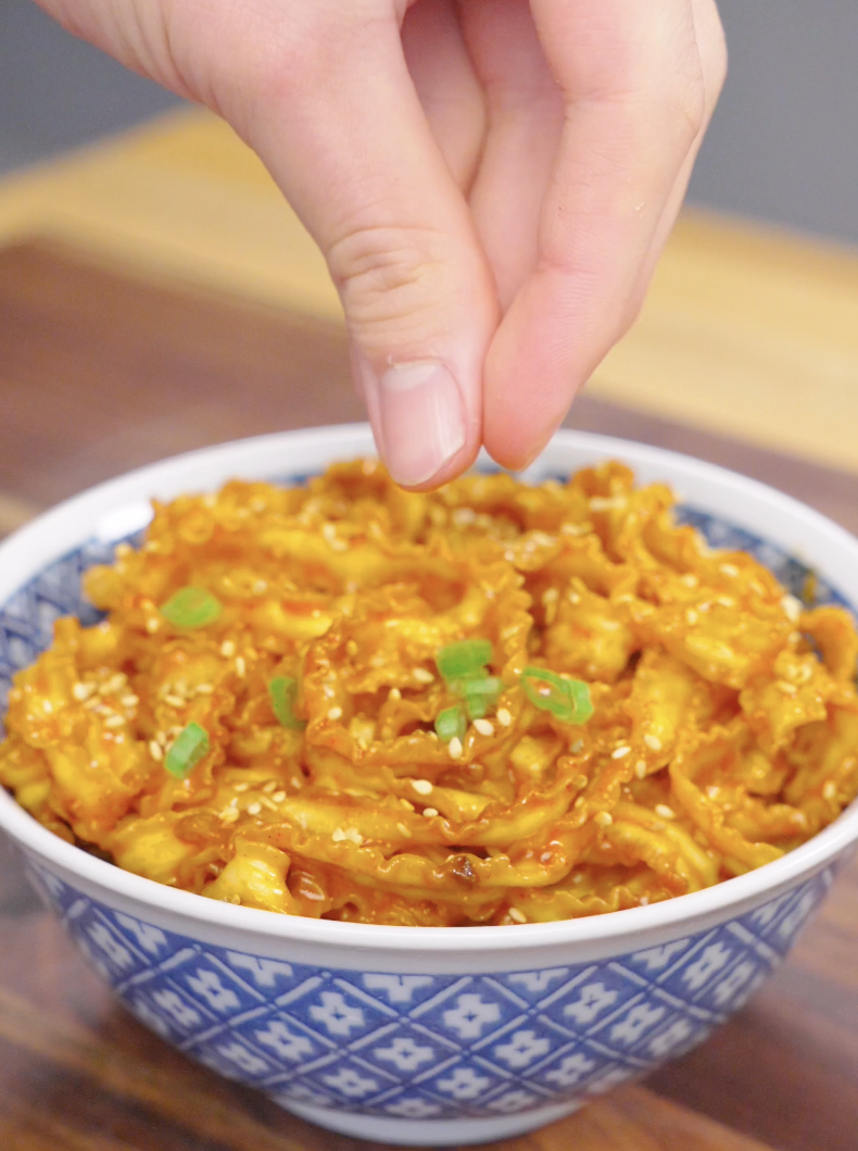 Fresh scallions being sprinkled over a bowl of Gochujang Butter Noodles before serving. The garnish adds freshness, color, and contrast to the creamy, spicy noodles.