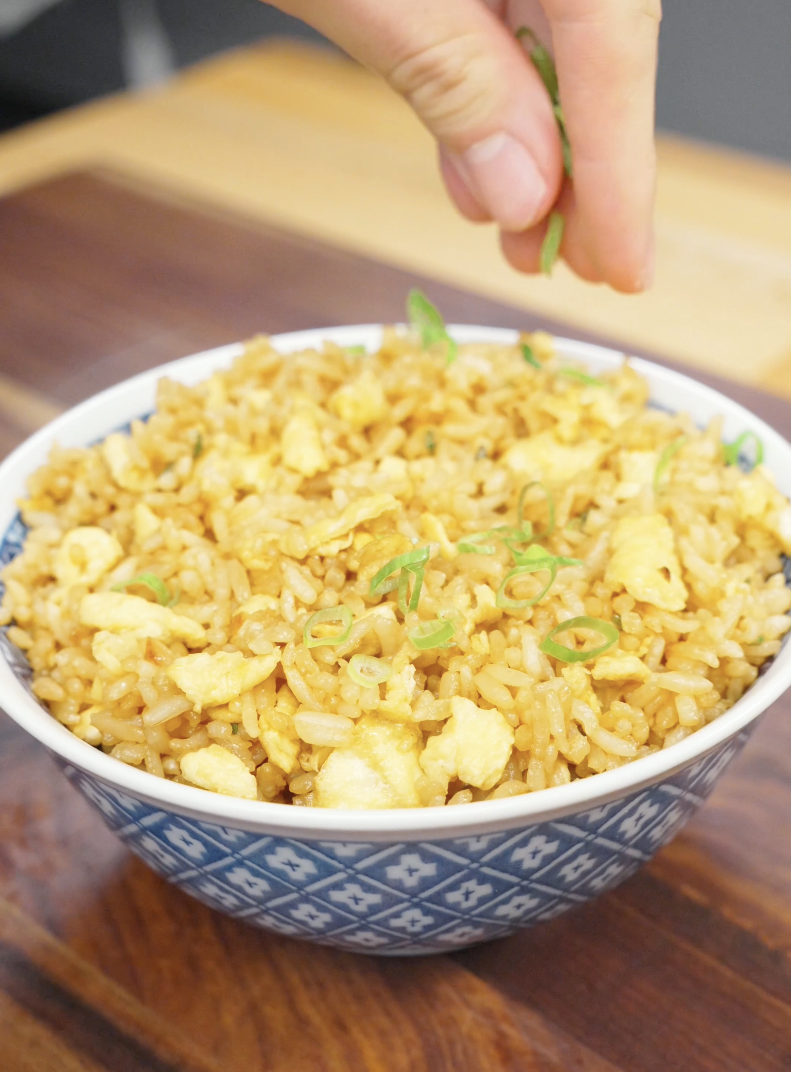 Fresh scallion greens being sprinkled over a bowl of Egg Fried Rice before serving. The garnish adds color, freshness, and a subtle onion flavor to this simple comfort food recipe.