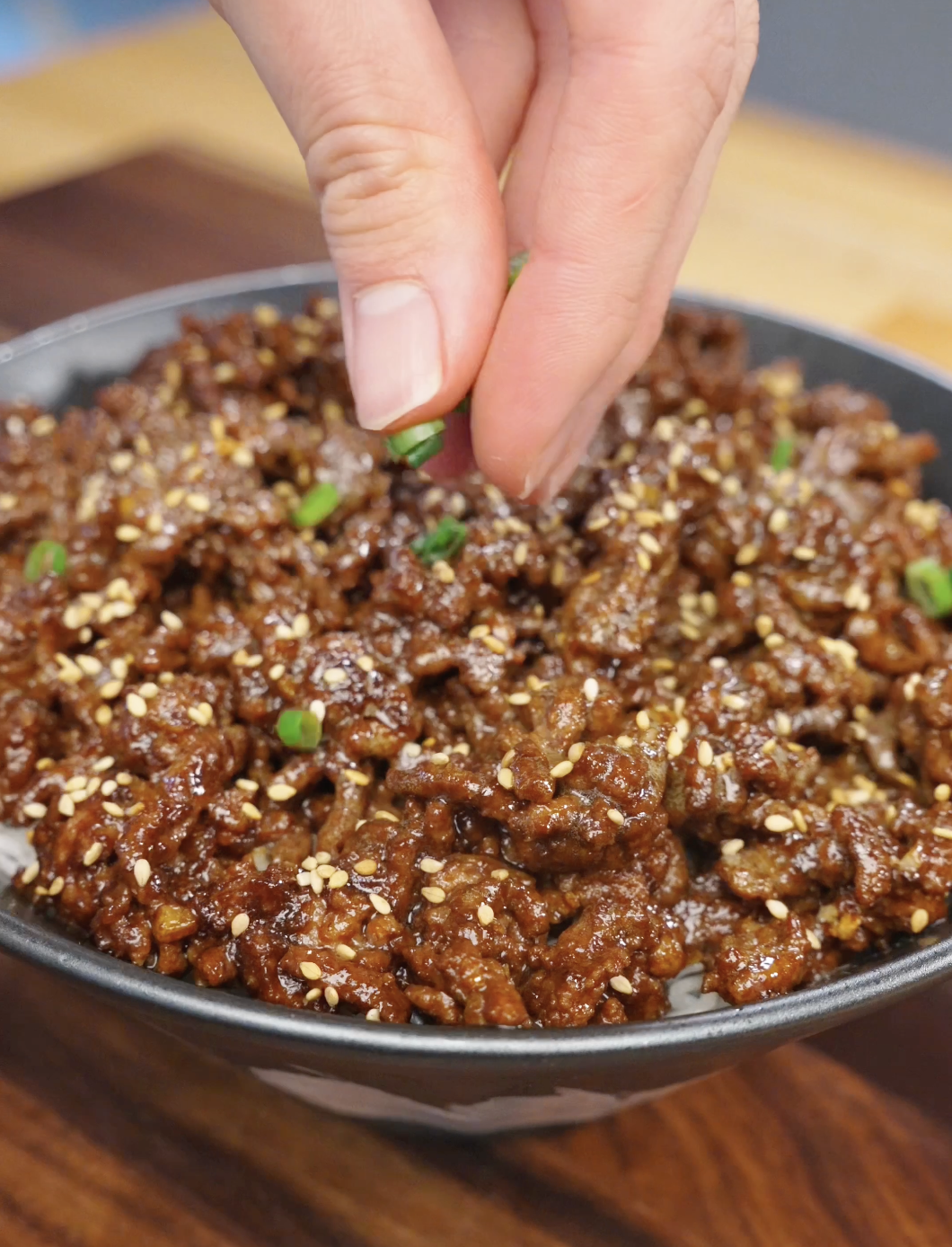 Fresh scallions being sprinkled over a bowl of Sticky Ground Beef Recipe topped with sesame seeds and served over white rice.