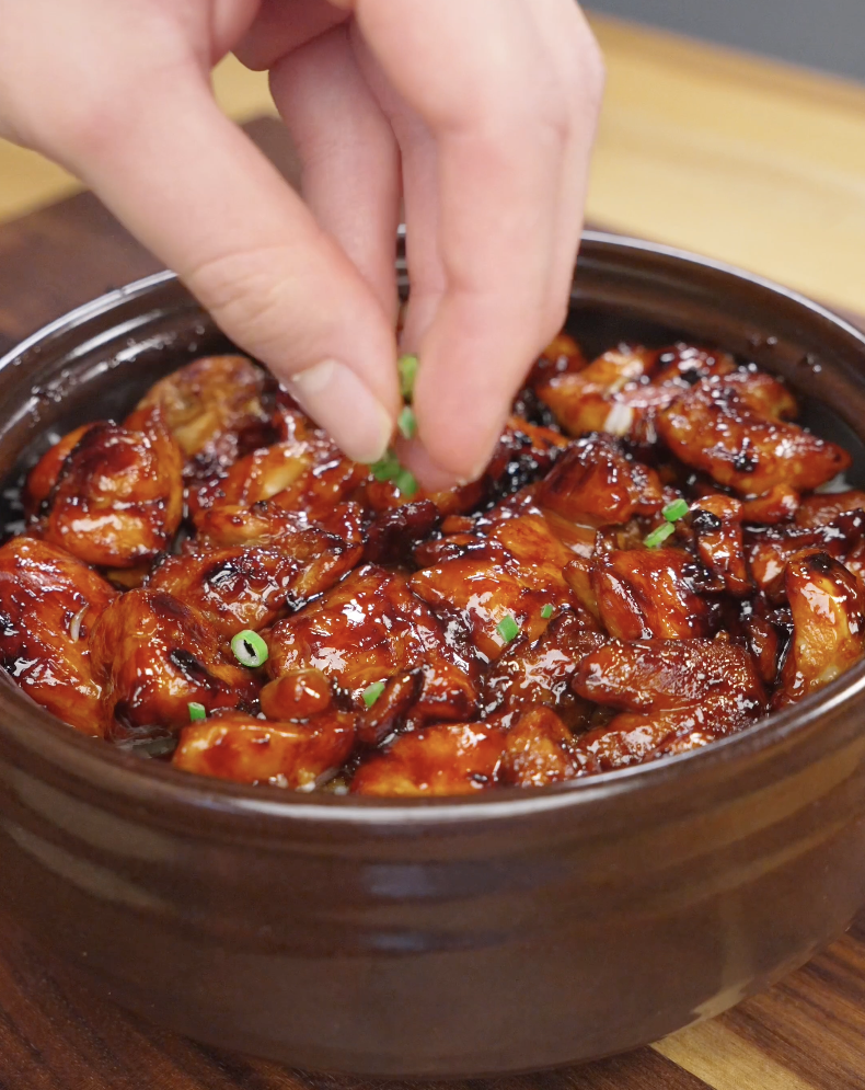 Fresh scallions being sprinkled over a bowl of Sticky Sweet Chicken coated in a glossy soy honey glaze. The garnish adds a fresh pop of color and flavor to this easy Asian-inspired chicken dinner.