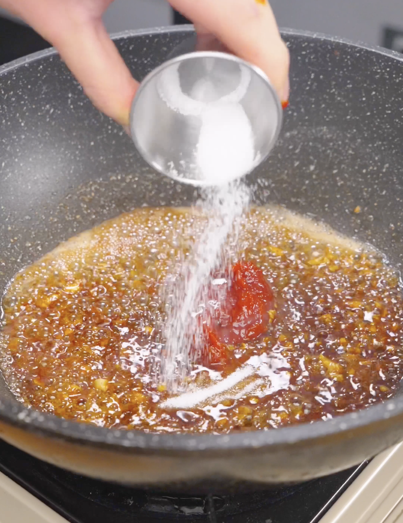 Sugar being added to a bubbling mixture of gochujang, soy sauce, garlic, and butter while preparing the sauce for Gochujang Butter Noodles. This combination creates a sweet, savory, and spicy glaze that coats every noodle.