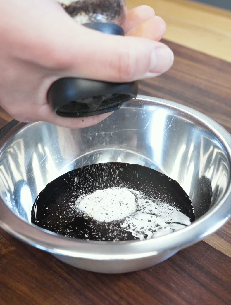 Black pepper being added into a bowl of soy sauce mixture to create the rich sauce for the Whole Garlic Chicken Stir Fry Recipe.