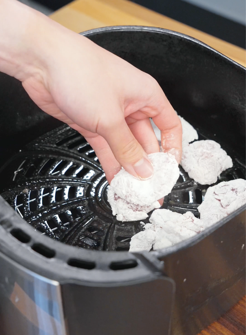 Breaded chicken thigh pieces being arranged in an air fryer basket before cooking. Spacing the chicken evenly allows hot air to circulate and create a crispy golden crust for this Crispy Hot Honey Chicken Recipe.