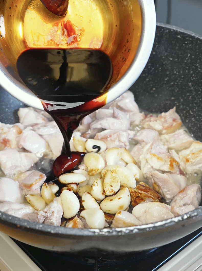 Thick soy-based sauce being poured over chicken thighs and softened garlic cloves in the Whole Garlic Chicken Stir Fry Recipe.