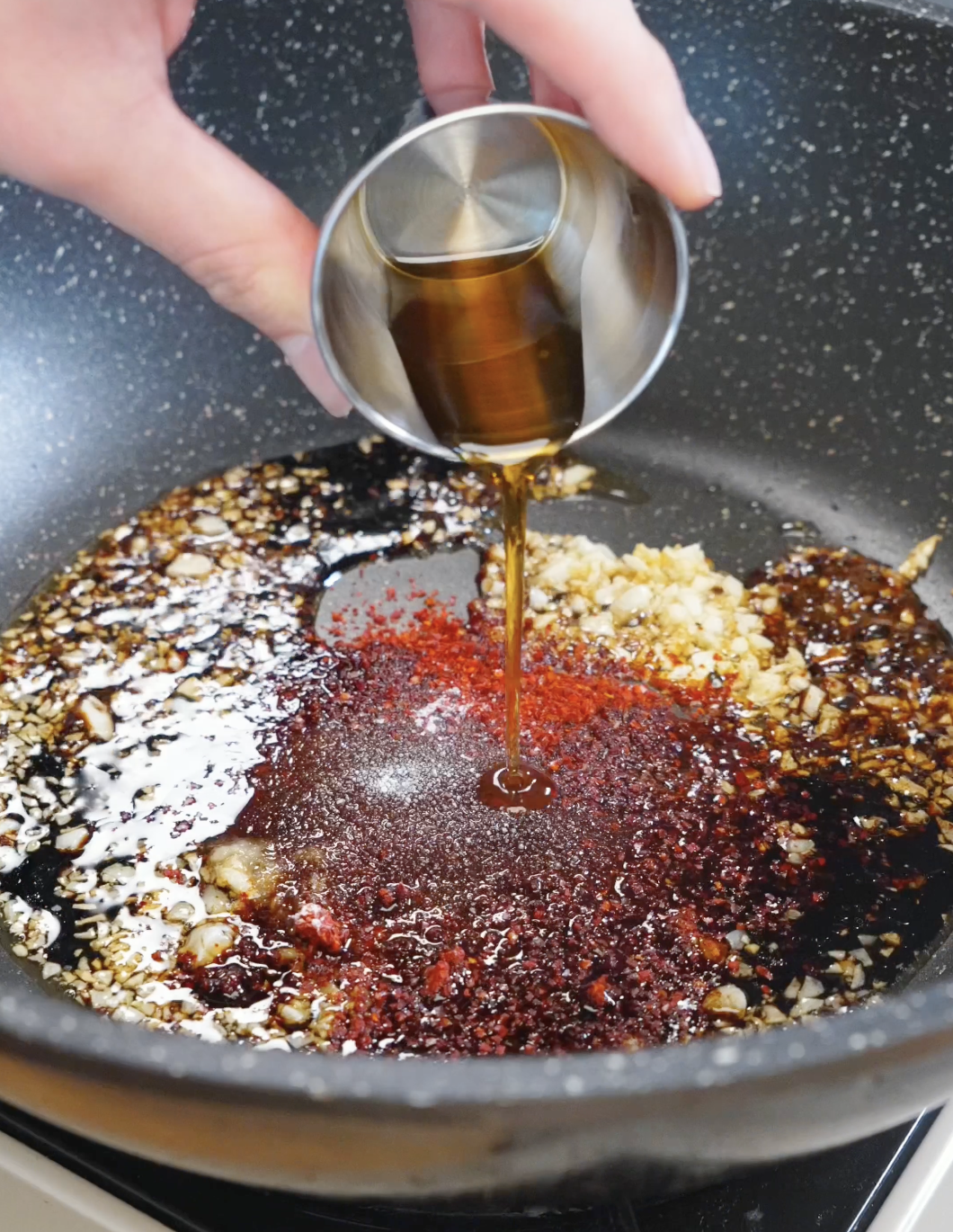Soy sauce and sesame oil being poured into a skillet with garlic and chili flakes to build the savory spicy sauce for this Spicy Garlic Noodles Recipe.
