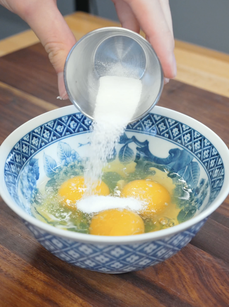 Sugar and salt being added to raw eggs before whisking for the Japanese Ground Beef Egg Bowl Recipe.