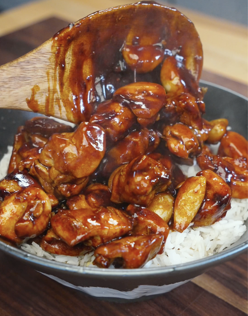 Saucy garlic chicken being spooned over steamed white rice with glossy whole garlic cloves in the Whole Garlic Chicken Stir Fry Recipe.