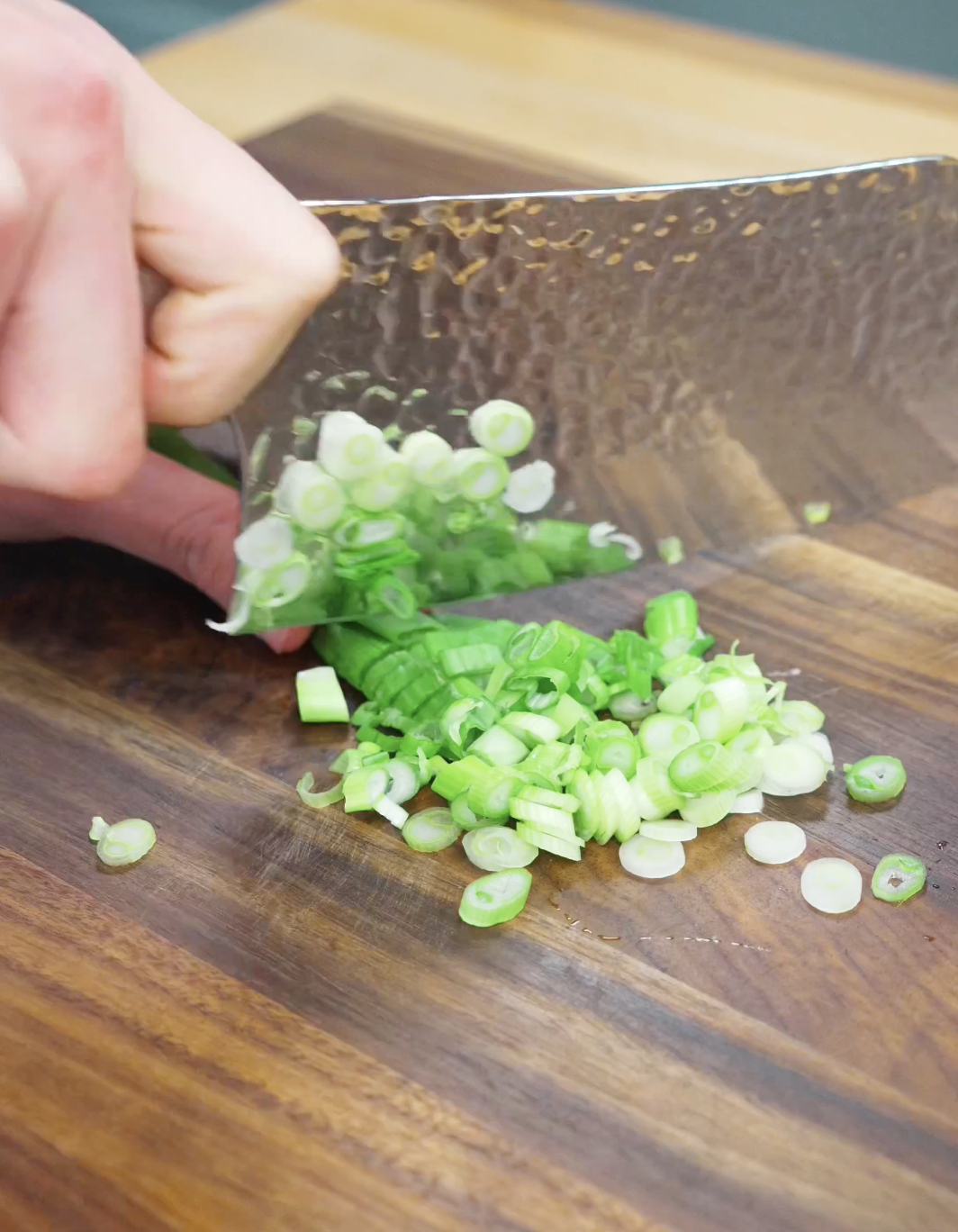 Fresh scallions being thinly sliced on a wooden cutting board to prepare aromatics for homemade Chili Oil Butter Fried Rice Recipe.