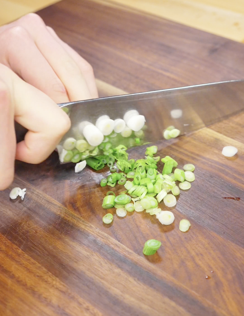 Fresh scallions being thinly sliced on a cutting board for Egg Fried Rice. Separating the scallion whites and greens helps build layers of flavor throughout the cooking process.