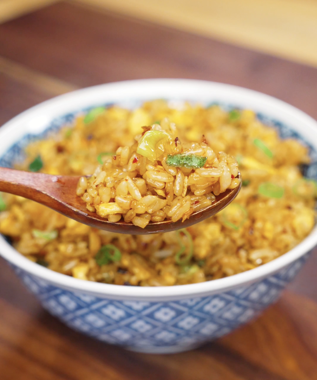 Wooden spoon lifting a bite of Chili Oil Butter Fried Rice filled with fluffy eggs, scallions, and glossy chili oil coated rice grains.