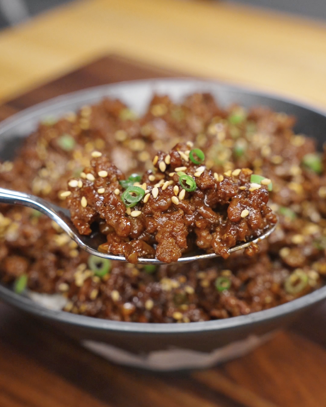 Spoon lifting glossy sticky ground beef coated in a savory sweet sauce and topped with sesame seeds and scallions.