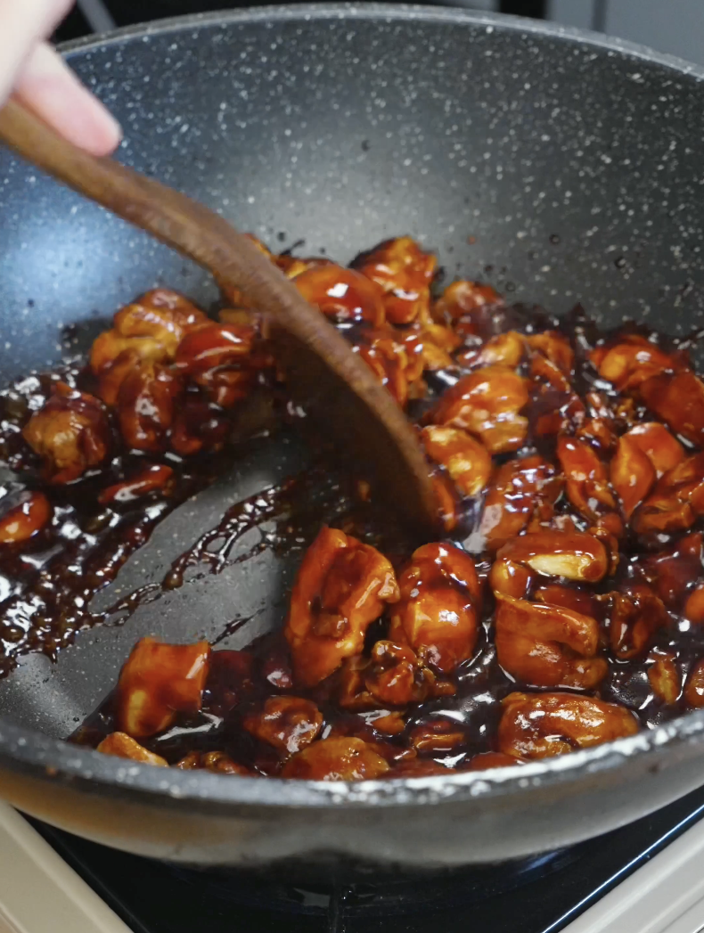 Chicken and whole garlic cloves being stirred in a glossy dark soy sauce until fully coated in the Whole Garlic Chicken Stir Fry Recipe.