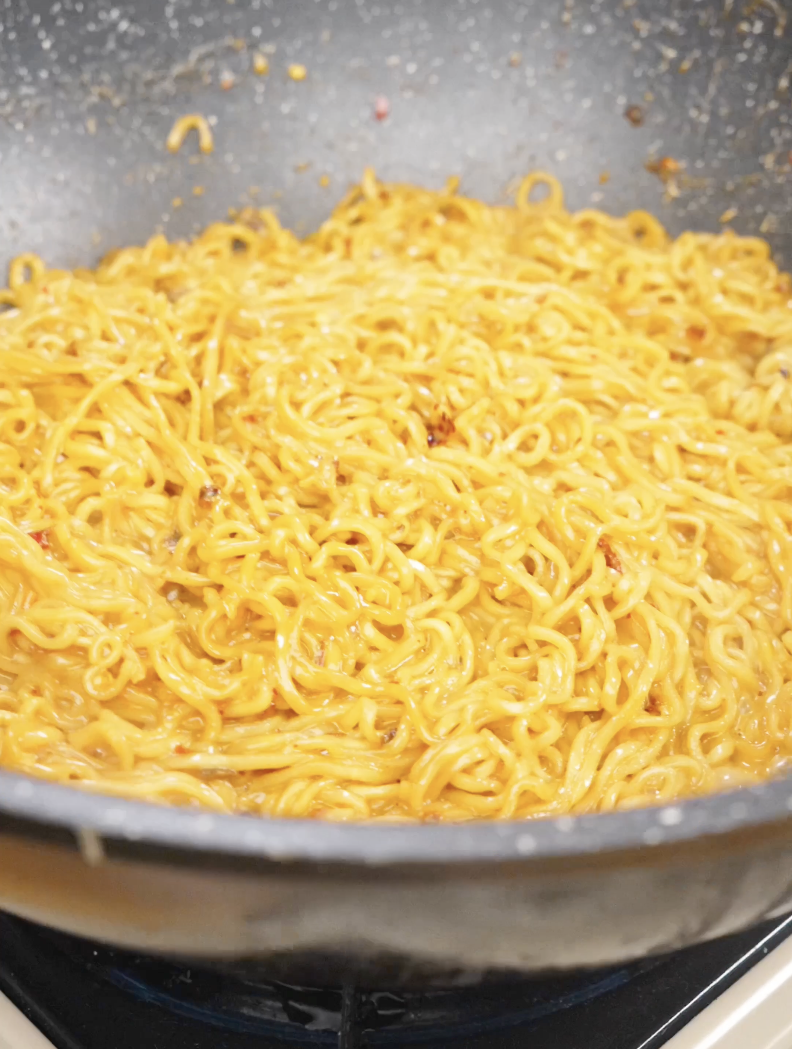 Noodles being tossed in a skillet with creamy chili oil sauce until thickened and evenly coated for this easy Creamy Chili Oil Noodles Recipe.